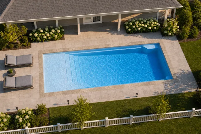 Daytime render of the Apollo 14 fiberglass pool with stone coping and a Sapphire Blue interior, seen from above at an angle.