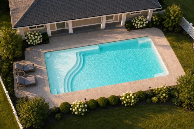 Daytime render of the Aspen 1635 fiberglass pool with stone coping and a Arctic Shimmer interior, seen from above at an angle.