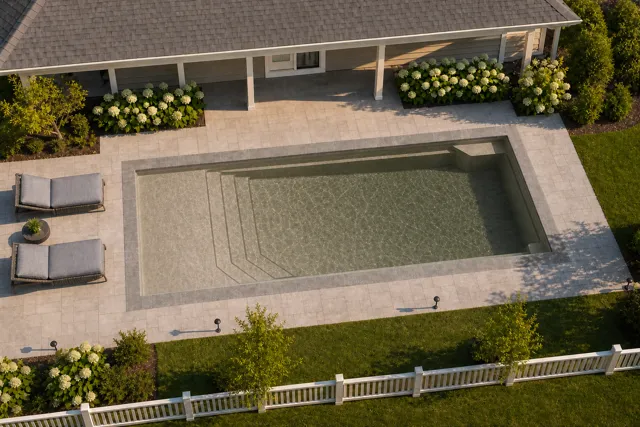 Daytime render of the Apollo 14 fiberglass pool with stone coping and a Coastal Bronze interior, seen from above at an angle.